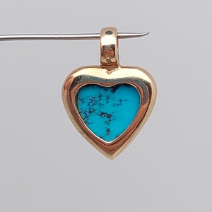 May include: A gold heart-shaped pendant with a turquoise stone set inside. The pendant has a bail at the top for attaching to a chain.