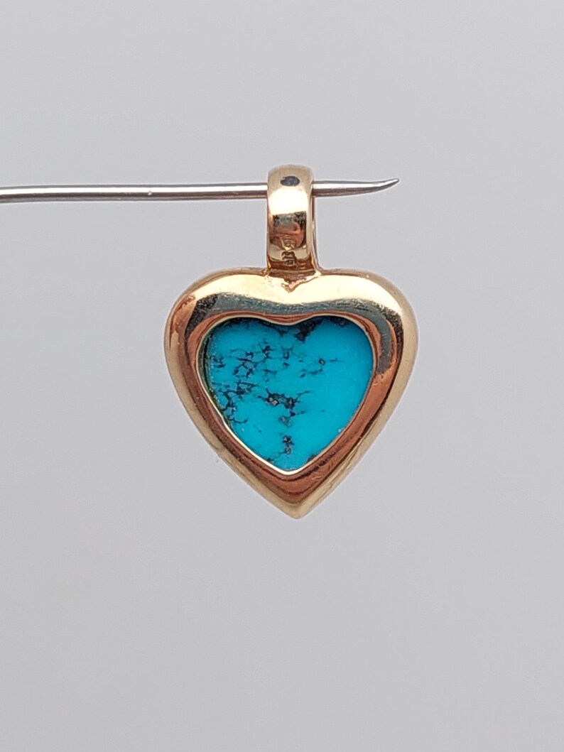 May include: A gold heart-shaped pendant with a turquoise stone set inside. The pendant has a bail at the top for attaching to a chain.