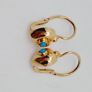 May include: A pair of gold-colored earrings with a turquoise stone set in each earring. The earrings have a lever back closure and a rounded design. The earrings are displayed on a white background.