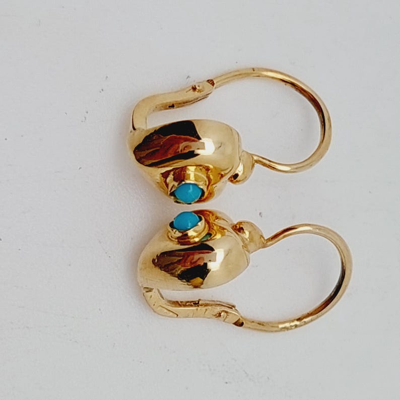 May include: A pair of gold-colored earrings with a turquoise stone set in each earring. The earrings have a lever back closure and a rounded design. The earrings are displayed on a white background.