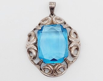 May include: A silver pendant with a large, faceted, light blue gemstone set in a decorative, filigree frame.