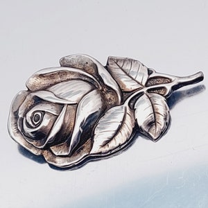 May include: A silver rose brooch with detailed leaves and a textured finish.