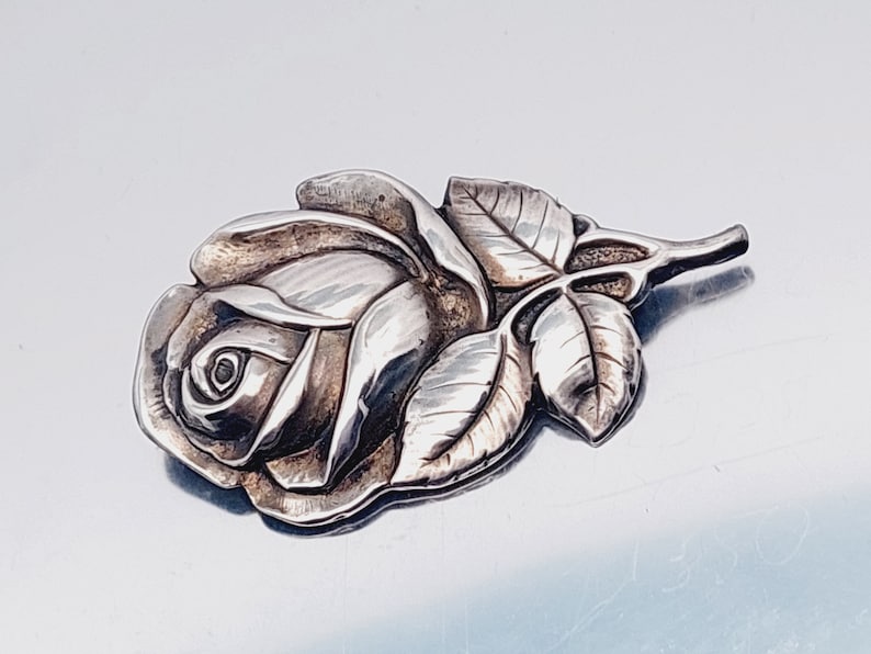 May include: A silver rose brooch with detailed leaves and a textured finish.