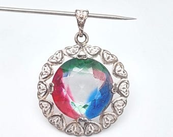 May include: A silver pendant with a large, multi-colored gemstone. The gemstone is round and features sections of red, green, and blue. The pendant is surrounded by a silver frame with heart-shaped cutouts.