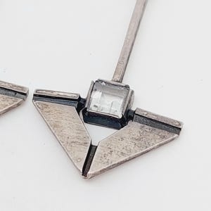 Puede incluir: Pendientes de plata con un dise&ntilde;o geom&eacute;trico de tri&aacute;ngulo y un cristal transparente en el centro.