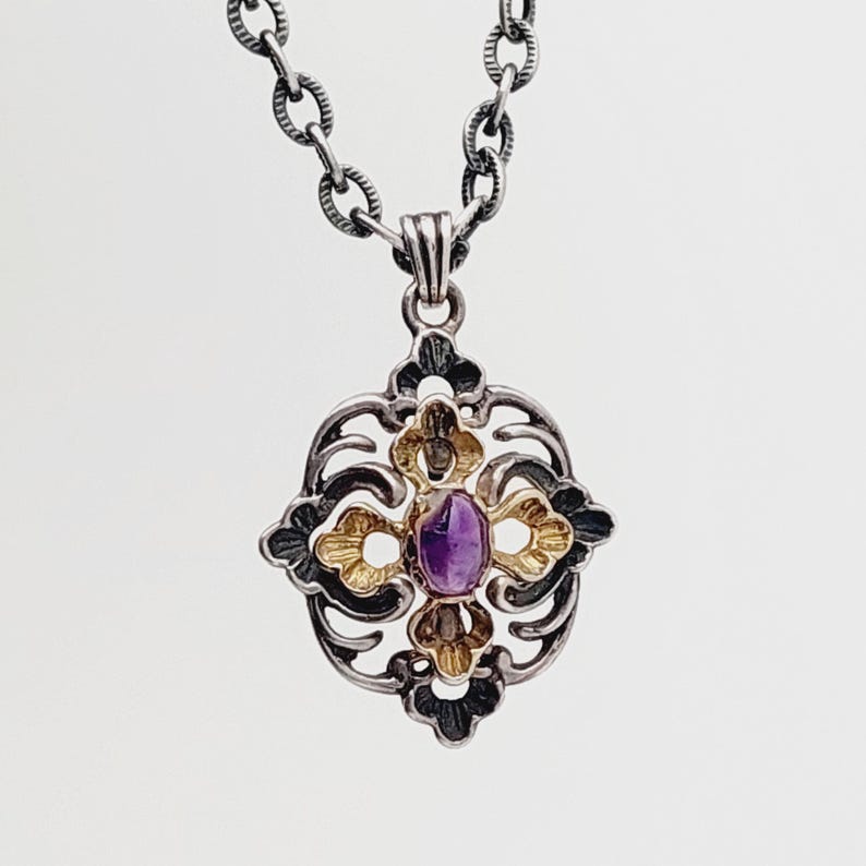 Puede incluir: Un collar de cadena de plata con un colgante que presenta una piedra preciosa p&uacute;rpura engastada en un dise&ntilde;o de filigrana de oro y plata.