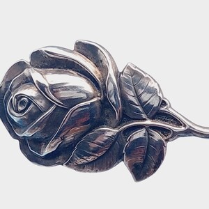 May include: A silver rose brooch with a detailed design of petals and leaves. The brooch has a pin on the back for attaching to clothing.