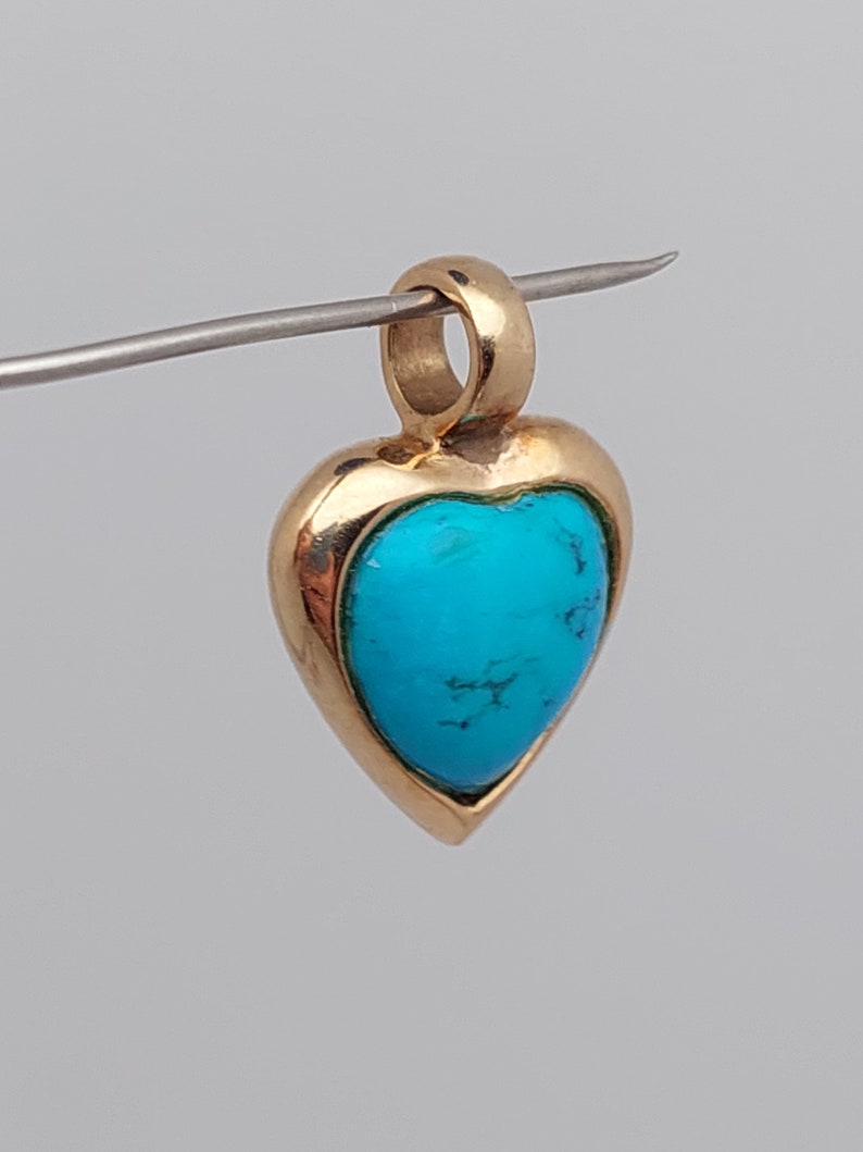 May include: A gold heart-shaped pendant with a turquoise stone set in the center.