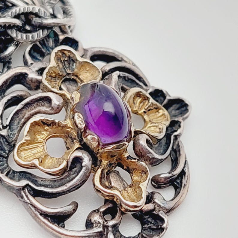Puede incluir: Un colgante de plata y oro con un dise&ntilde;o intrincado que presenta una piedra preciosa de amatista p&uacute;rpura.