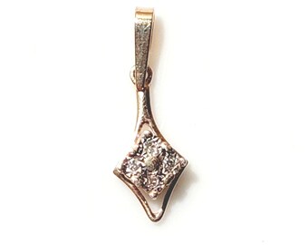 May include: A gold-toned pendant with a diamond-shaped cluster of small stones. The pendant has a delicate, elongated design with a loop at the top for a chain. The stones sparkle against the gold setting.