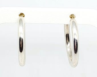 May include: A pair of polished silver hoop earrings with a smooth, rounded profile. The earrings feature a simple circular design with a reflective metallic finish and a secure post-back closure mechanism, presenting a clean and classic appearance.