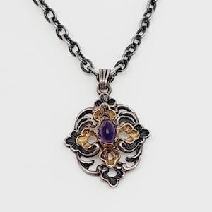 Puede incluir: Un collar de cadena de plata con un colgante que presenta una piedra preciosa p&uacute;rpura engastada en un dise&ntilde;o de filigrana de oro y plata.