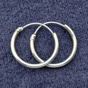 Può includere: Un paio di orecchini a cerchio d'argento. Gli orecchini sono semplici e classici e sarebbero un'ottima aggiunta a qualsiasi collezione di gioielli.
