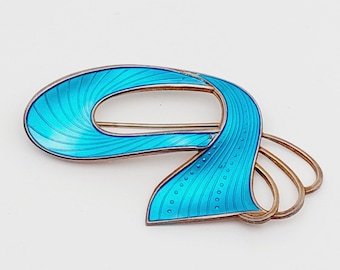 May include: A blue and silver abstract brooch with a swirling design. The brooch is made of sterling silver and enamel.