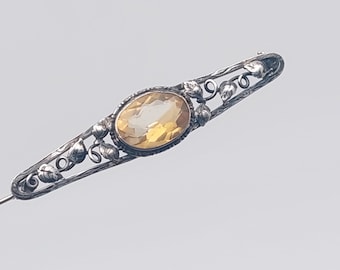 May include: A silver brooch with a yellow gemstone set in a floral design.