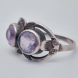 May include: A silver ring with two light purple gemstones set in a floral design.