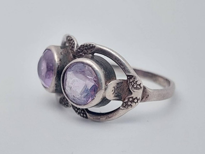May include: A silver ring with two light purple gemstones set in a floral design.