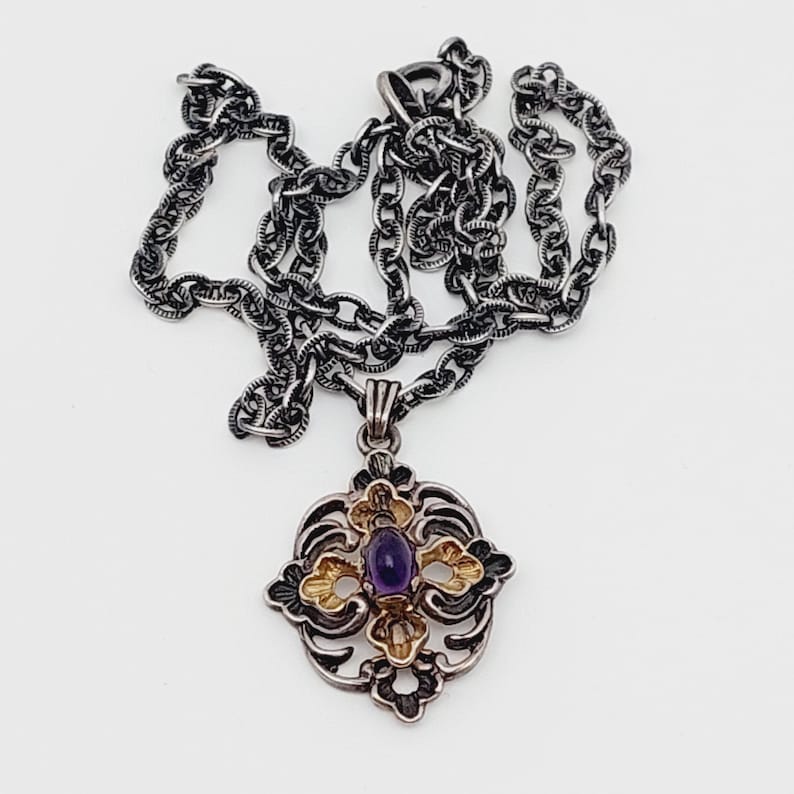 Puede incluir: Un collar de cadena de plata con un colgante que presenta una piedra preciosa p&uacute;rpura engastada en un dise&ntilde;o de filigrana de oro y plata.