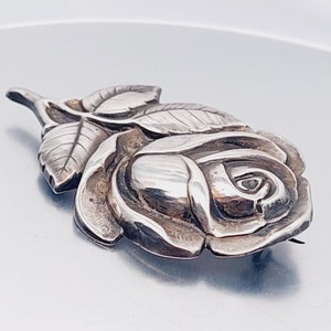 May include: A silver rose brooch with detailed leaves and a textured finish.