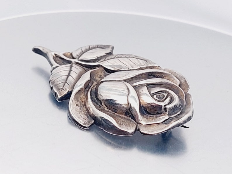 May include: A silver rose brooch with detailed leaves and a textured finish.