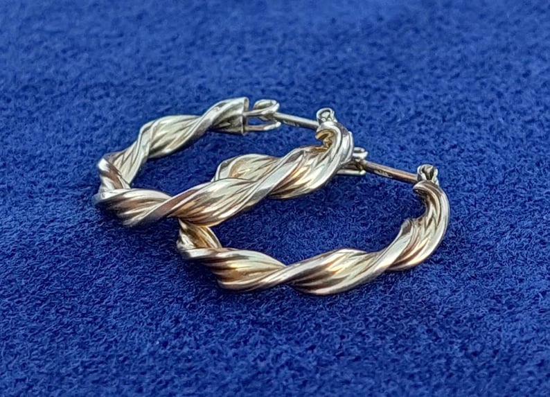 Puede incluir: Un par de pendientes de aro retorcidos en oro y plata. Los pendientes son de metal y tienen un acabado pulido.