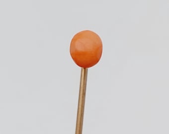 May include: A single orange glass bead on a gold pin.