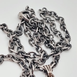 Puede incluir: Un collar de cadena de plata con un dise&ntilde;o de eslab&oacute;n texturizado de forma ovalada. La cadena tiene un cierre de mosquet&oacute;n.