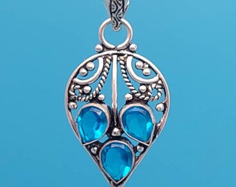 May include: Silver pendant with a teardrop shape and intricate filigree design. Three blue gemstones are set in the center of the pendant.