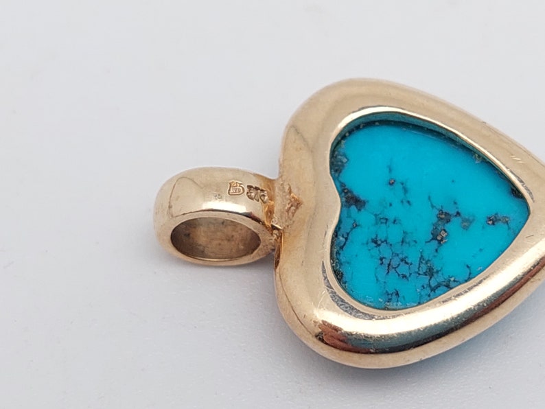 May include: Gold heart-shaped pendant with a turquoise stone set in the center. The pendant has a bail for attaching to a chain.