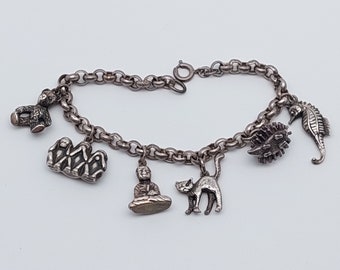May include: A silver charm bracelet with a variety of charms, including a teddy bear, a group of monkeys, a meditating figure, a cat, a seahorse, and a spiky ball.