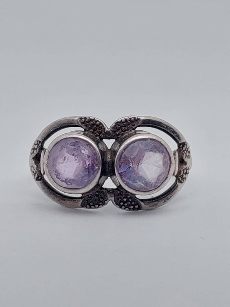 May include: A silver ring with two round, light purple gemstones set in a delicate, floral design.