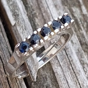 May include: A silver ring with five black gemstones set in a row. The ring is on a wooden surface.