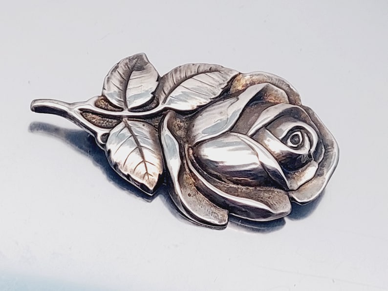 May include: A silver rose brooch with detailed leaves and a textured finish.