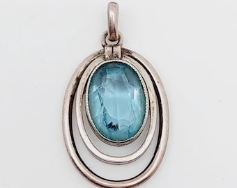 May include: A silver pendant with a light blue oval gemstone set in a double circle design.