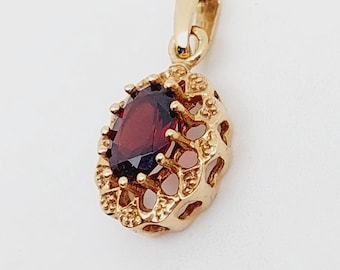 Puede incluir: Un colgante de oro con una piedra preciosa roja engastada en un marco delicado y adornado.