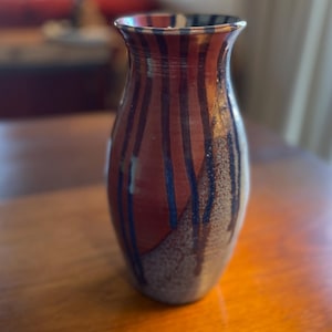 May include: A ceramic vase with a red, blue, and white striped design. The vase has a rounded bottom and a narrow neck.
