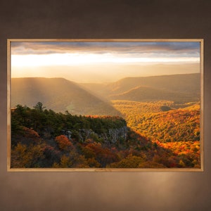 May include: A panoramic view of a mountain range with a cliff face in the foreground. The trees are a mix of green and orange, with the sun shining through the clouds.