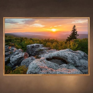 May include: A scenic landscape photograph of a rocky mountaintop at sunset. The sun is setting behind the mountains, casting a warm glow over the scene. The rocks are covered in moss and lichen, and there are trees in the foreground.