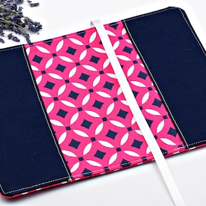 May include: A pink and navy blue fabric book cover with a geometric pattern and a white ribbon bookmark.