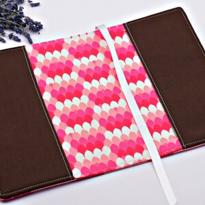 May include: A brown fabric book cover with a pink and white patterned design. The cover has a white ribbon bookmark.