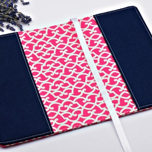 May include: A pink and white patterned book cover with a navy blue fabric border and a white ribbon bookmark.