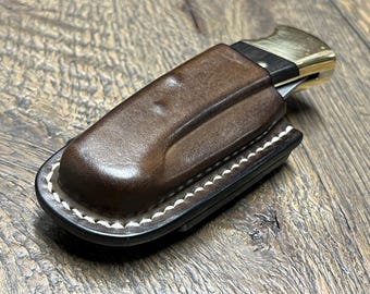 Peut inclure: Un étui à couteau en cuir marron avec des coutures blanches. L'étui a un rabat qui recouvre la lame du couteau et un accent en laiton sur le dessus.