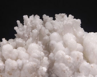 Può includere: Un gruppo di formazioni minerali bianche a forma di cavolfiore. Il minerale ha una superficie ruvida e testurizzata.