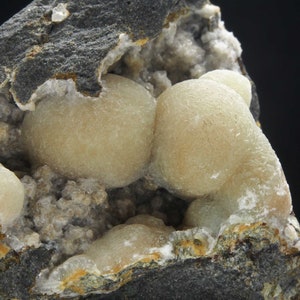 Może przedstawiać: Zbliżenie na skałę z skupiskiem zaokrąglonych, jasnobrązowych formacji mineralnych. Formacje mineralne znajdują się w zagłębieniu w skale.