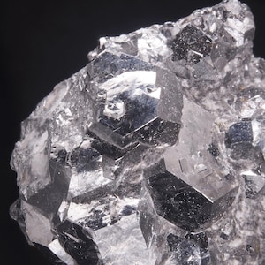 Può includere: Un gruppo di cristalli grigi metallici sfaccettati con una superficie riflettente. I cristalli sono disposti in modo casuale, creando una texture unica e interessante.