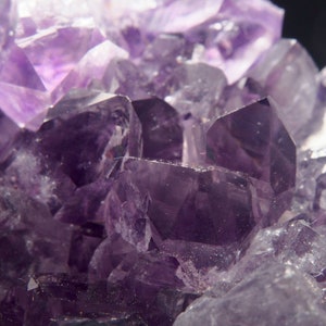 May include: Close-up of a cluster of amethyst crystals. The crystals are a deep purple colour and have a variety of shapes and sizes. The crystals are arranged in a cluster, with some of the crystals overlapping each other.
