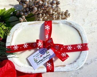 May include: A white wooden dough bowl filled with a white soy candle. The candle is tied with a red ribbon with white snowflakes and a tag that reads "the little norwegian candle company Saratoga Christmas 8 oz soy candle Malta NY".
