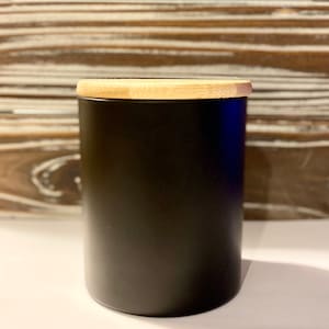 Op de afbeelding: Een zwarte keramische pot met een bamboe deksel. De pot is cilindrisch en heeft een gladde, matte afwerking.