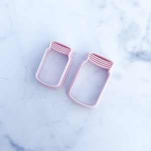 Puede incluir: Dos cortadores de galletas de plástico rosa en forma de tarros de cristal.