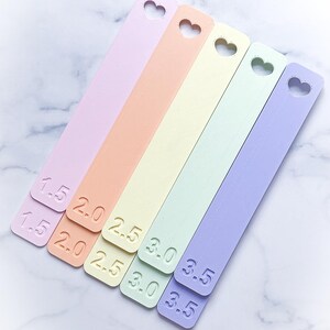 May include: Five pastel-colored measuring sticks with heart cutouts. The sticks are labeled with numbers from 1.5 to 3.5.